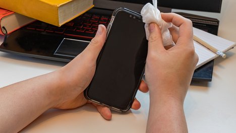 Das Foto zeigt ein Smaretphone, das mit einem Desinfektionstuch gereinigt wird. 